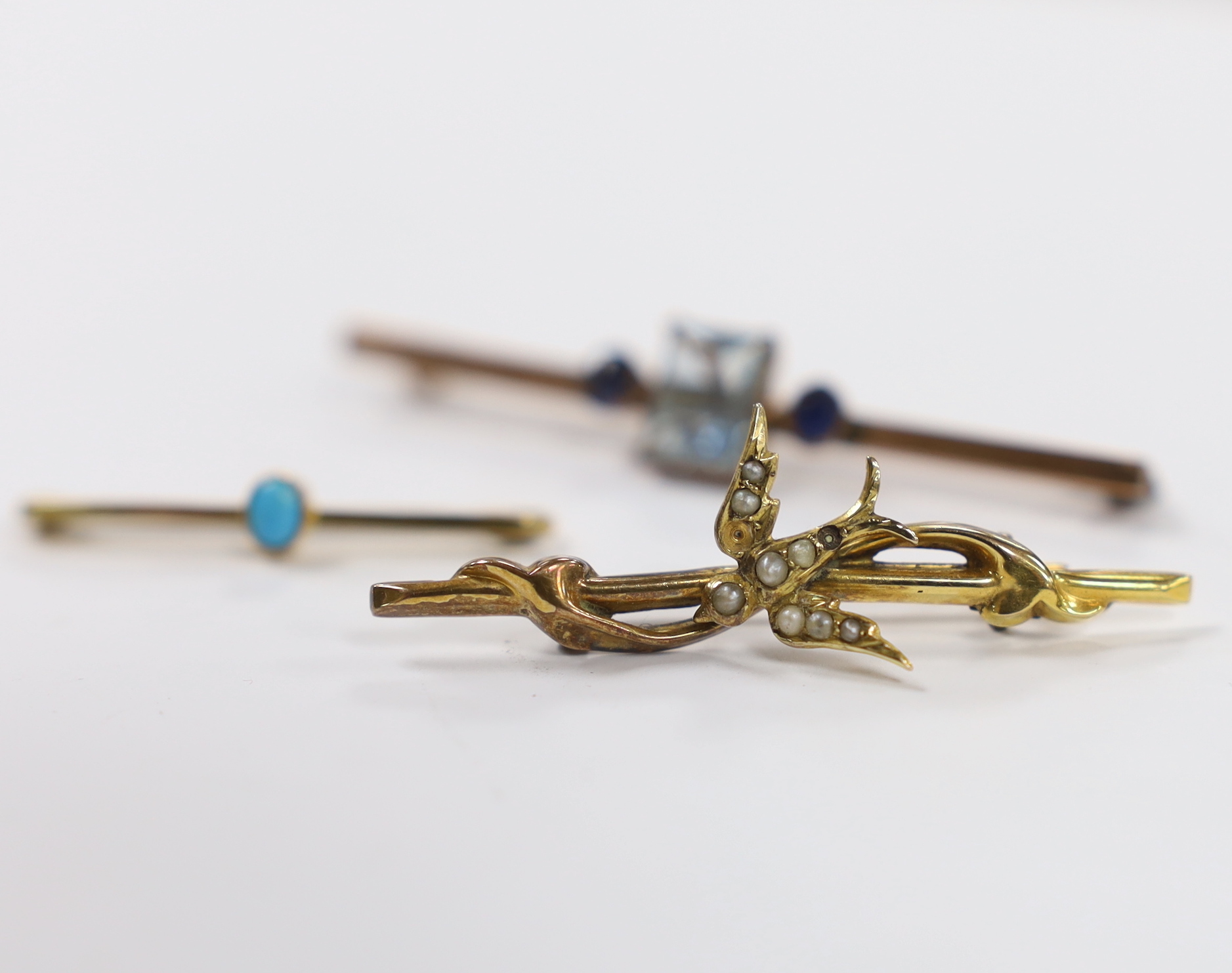 An Edwardian 9ct gold and seed pearl set swallow bar brooch, 43mm, a 9ct gold and turquoise set tie pin and a yellow metal, single stone aquamarine and two stone sapphire set bar brooch.